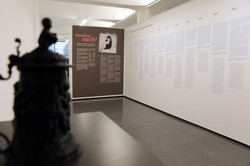 Ausstellungsansicht aus ‚Benehmt euch‘ im Dortmunder U: Im Vordergrund die Silhouette einer Skulptur, dahinter Wände mit Schrifttafeln.