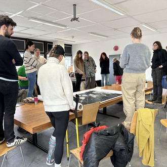 Studierende und Lehrende stehen um einen Tisch auf dem Zeichnungen liegen