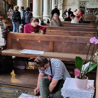 Menschen sitzen verteilt in den Kirchenbänken einer Kirche und zeichnen.