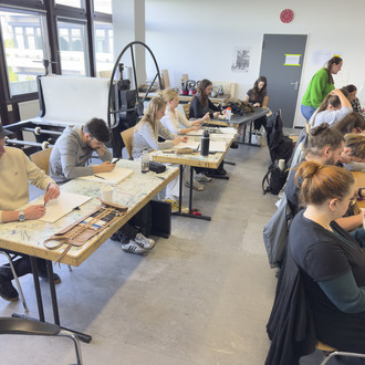 Studierende sitzen an Tischen und zeichnen