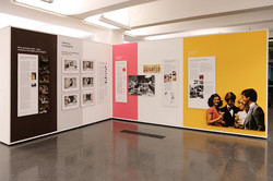 Ausstellungsansicht aus ‚Benehmt euch‘ im Dortmunder U: Schrifttafeln und Bilder von Menschengruppen an bunten Wänden.