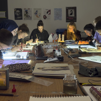 Studierende sitzen um einen Tisch und zeichnen