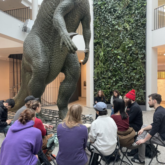 Studierende sitzen um Dinosaurier Statur