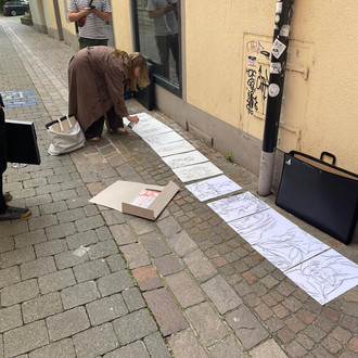 eine Studierende reiht Zeichnungen auf dem Boden vor einer Hauswand auf