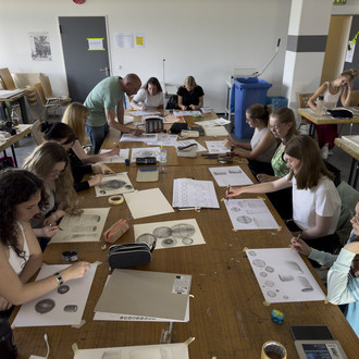 Studierende sitzen um einen Tisch und zeichnen