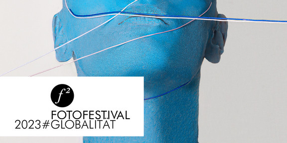 Das Plakat der Fotoausstellung zeigt den Kopf einer Person, die blau angemalt ist und mit Schnürren umbunden ist.