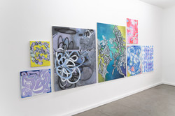 Schrägansicht einer Wand im Superraum Dortmund mit abstrakten Gemälden in Blau-, Grau-, Grün- und Rosatönen, unterschiedlich groß gehängt, Ausstellung TPLI III.