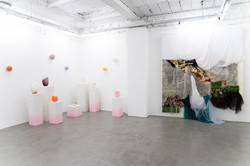 Eckansicht im Ausstellungsraum Superraum Dortmund: mehrere kleine, farbige Glasobjekte auf weißen Sockeln mit rosa Farbverlauf, an der Wand eine großformatige textile Installation, Ausstellung TPLI III.