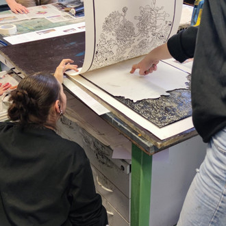 Studierende betrachten Drucke auf einem Tisch