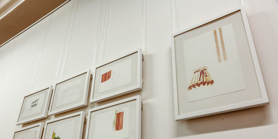 Sieben gerahmte Bilder hängen in einer Ausstellung an der Wand.