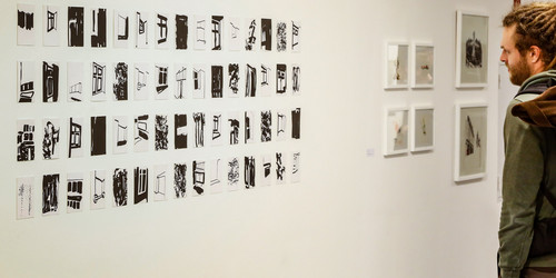 Ein Mann betrachtet kleine Drucke an der Wand in einer Ausstellung.